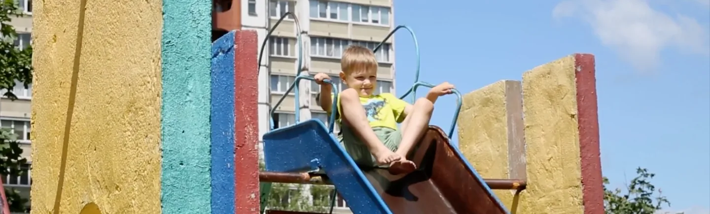 Ein Kind klettert auf einem Spielplatz vor Plattenbauten